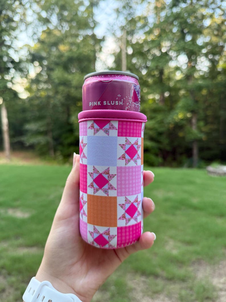 Puede incluir: Un enfriador de latas rosa y naranja con un patr&oacute;n de patchwork de cuadrados con motivos de estrellas y dise&ntilde;os a cuadros. El enfriador sostiene una lata de metal con una etiqueta rosa que muestra claramente el texto PINK SLUSH en letras blancas.