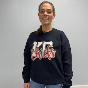 May include: A black sweatshirt with a gold and red glitter design that says "KC Chiefs".