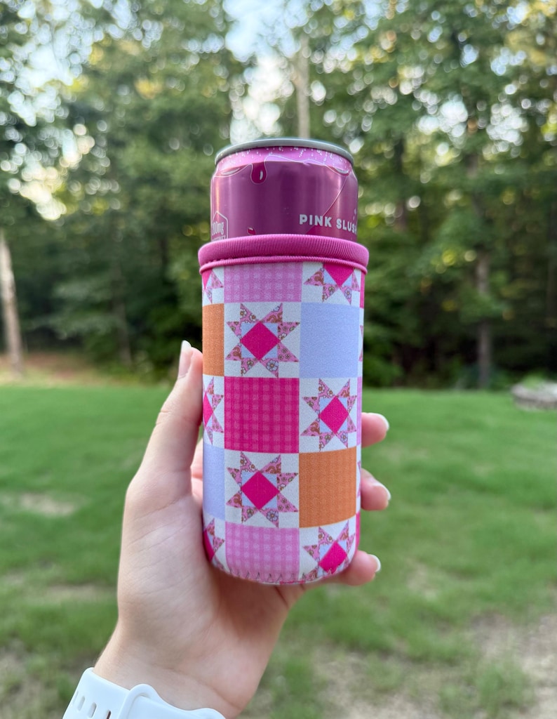 Puede incluir: Una funda de neopreno para latas con un patr&oacute;n de patchwork repetitivo en tonos rosa, naranja y morado claro. El dise&ntilde;o incluye cuadrados alternos de colores s&oacute;lidos, cuadros vichy y motivos de estrellas florales. La parte superior es rosa.