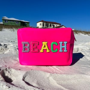 May include: A bright pink beach bag with the word "BEACH" embroidered in colorful letters.