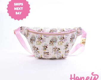 May include: A pink fanny pack with a white background and a pattern of Mickey Mouse and Minnie Mouse characters. The pack has a gold zipper and a pink adjustable strap.