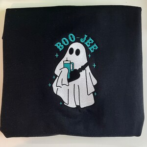 May include: Black sweatshirt with a white ghost holding a teal cup and the text "BOO-JEE" in teal.