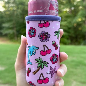 May include: A light purple neoprene can cooler sleeve featuring a repeating pattern of pink hibiscus flowers, red cherries, green palm trees, blue dolphins, purple starfish, and red strawberries, holding a pink slush beverage can.