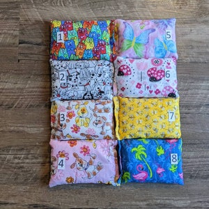 May include: An assortment of eight small, rectangular fabric items with various colorful patterns. Designs include cats, dogs, butterflies, ladybugs, bees, and tropical themes. Each item is numbered from 1 to 8.