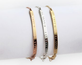 May include: Three gold, silver, and rose gold bracelets with engraved coordinates. The coordinates are 34.0522 -118.2431, 59.7392 -104.9903, and 29.4406 -79.9569.