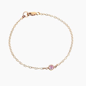 Könnte beinhalten: Ein zartes Armband aus einer goldenen Kette mit einem einzigen rosafarbenen Edelstein.