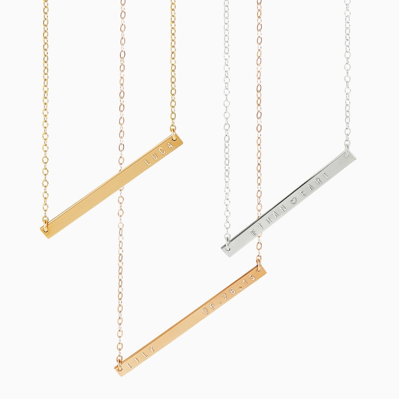 May include: Three gold bar necklaces with personalized engravings. The top necklace reads "LUCA", the middle necklace reads "LILY 06.26.15", and the bottom necklace reads "ETHAN & FARL" with a heart symbol.