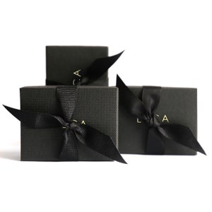 Puede incluir: Tres cajas de regalo negras con lazos de cinta negra y letras doradas que dicen "LCA" en cada caja.
