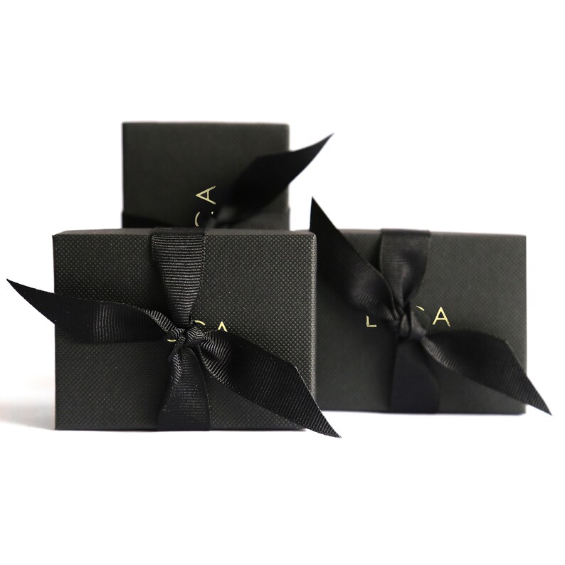 Puede incluir: Tres cajas de regalo negras con lazos de cinta negra y letras doradas que dicen "LCA" en cada caja.