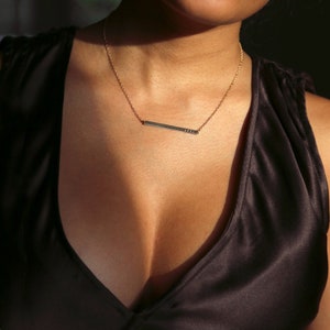 May include: A gold chain necklace with a thin, horizontal bar pendant. The bar is engraved with the word "LOVE". The necklace is worn by a person with a low-cut neckline.