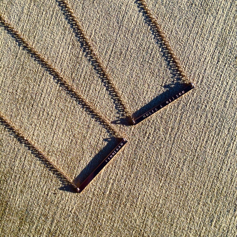 May include: Three gold necklaces with bar pendants. The pendants have the words "BREATHE", "JUST IS A HELLSO", and "CHLOE" engraved on them.