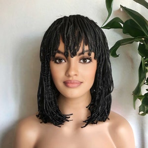 May include: A black braided wig with a fringe. The wig is styled in a bob shape and has a natural look.