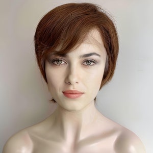 Puede incluir: Una peluca corta de color marrón con raya lateral y flequillo. La peluca está peinada con un estilo bob moderno y elegante.