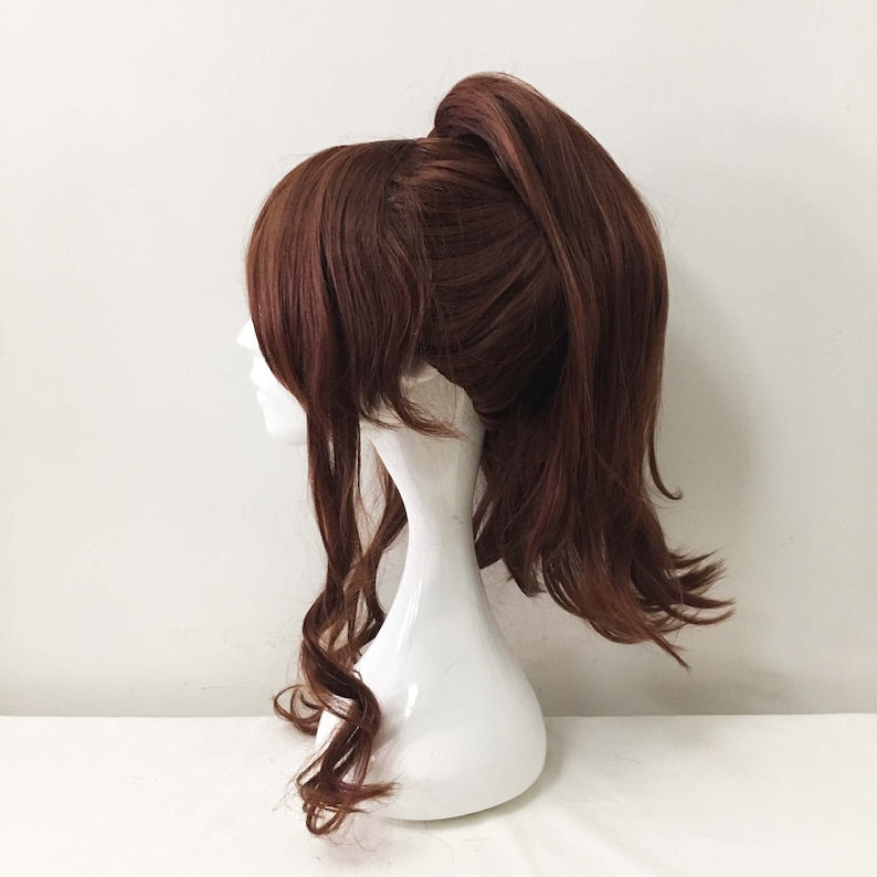 K&ouml;nnte beinhalten: Eine lange, braune Per&uuml;cke mit einem hohen Pferdeschwanz. Die Per&uuml;cke hat lockere Locken um das Gesicht und ist in einem l&auml;ssigen, allt&auml;glichen Look gestylt.