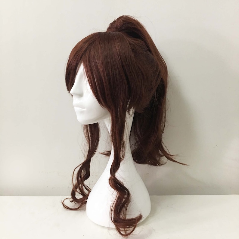 K&ouml;nnte beinhalten: Eine braune Per&uuml;cke mit langen, lockigen Haaren, die zu einem hohen Pferdeschwanz gebunden sind. Die Per&uuml;cke befindet sich auf einem wei&szlig;en Mannequin-Kopf.