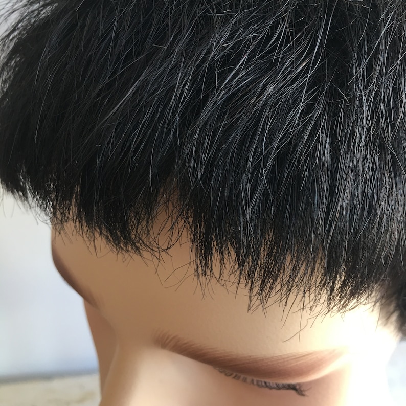 May include: Close-up of a person's black hair, styled in a short, straight cut. The hair is parted on the side and falls just above the forehead.