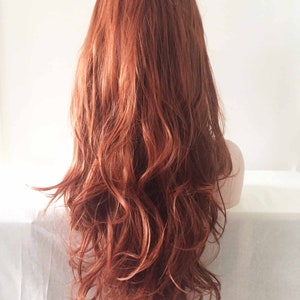 May include: A long, wavy wig in a warm auburn color. The wig features a natural-looking style with loose curls and a layered cut. The hair cascades down the back, creating a voluminous and flowing appearance. The wig is styled on a mannequin head.