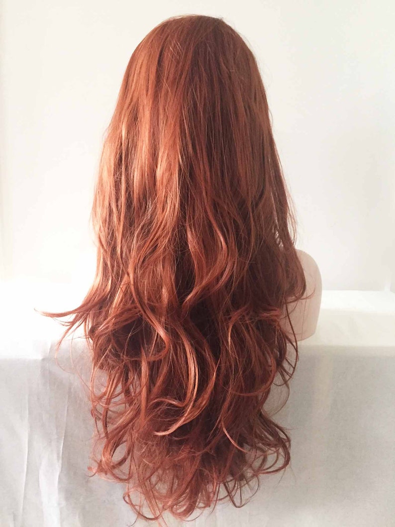 May include: A long, wavy wig in a warm auburn color. The wig features a natural-looking style with loose curls and a layered cut. The hair cascades down the back, creating a voluminous and flowing appearance. The wig is styled on a mannequin head.