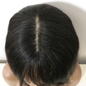 May include: A black wig with a center part. The wig is made of human hair and has a natural look.