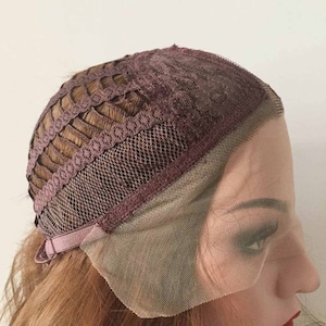 May include: A close-up of a wig cap with brown hair. The cap features a dark brown lace front and a dark brown lace top. The wig cap has a brown adjustable strap.