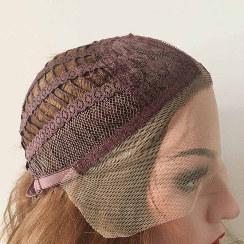 May include: A close-up of a wig cap with brown hair. The cap features a dark brown lace front and a dark brown lace top. The wig cap has a brown adjustable strap.