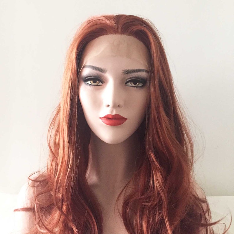 May include: A mannequin head with a long, wavy auburn wig. The wig features a natural-looking hairline and is styled with loose curls. The mannequin has full makeup, including red lipstick and defined eyebrows. The overall look is glamorous and ready to wear.
