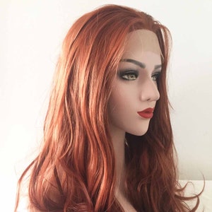 May include: A mannequin head with a long, wavy, auburn wig. The wig has a lace front and is styled with loose waves. The mannequin has red lipstick and dark eye makeup. The background is plain white.