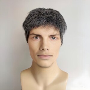 May include: A mannequin head with a realistic face and short, gray hair. The mannequin has a neutral expression and is set against a plain white background. The skin tone is light, and the hair is styled in a short, layered cut.