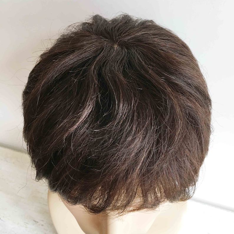 May include: A close-up of a dark brown wig with a short, layered style. The wig is styled with a side part and has a natural, realistic look.