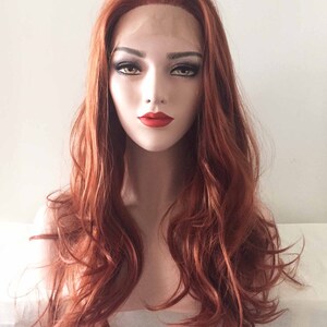 May include: A red-orange wig with long, wavy hair. The wig features a lace front and is styled with loose curls. The mannequin head has full makeup, including red lipstick and dark eye makeup. The background is a plain white.