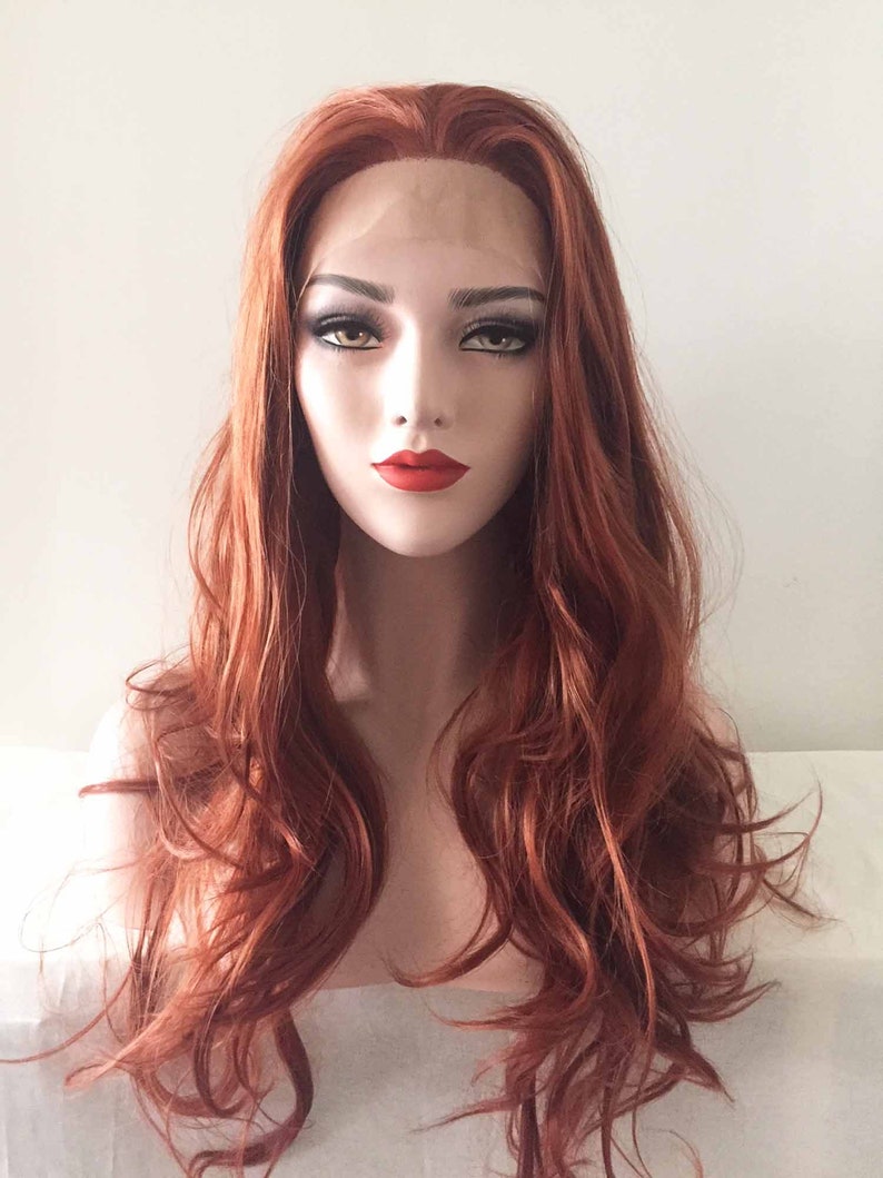 May include: A red-orange wig with long, wavy hair. The wig features a lace front and is styled with loose curls. The mannequin head has full makeup, including red lipstick and dark eye makeup. The background is a plain white.