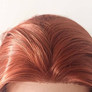 May include: Close-up of a reddish-brown wig with a lace front. The synthetic hair is styled with long, flowing strands. The wig's base is a light beige color, and the hair has a natural-looking sheen.