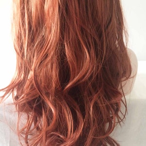 May include: A close-up view of wavy, auburn-colored hair. The hair is styled with loose waves, and the color has a mix of red and brown tones. The hair appears to be healthy and shiny, with a natural look.