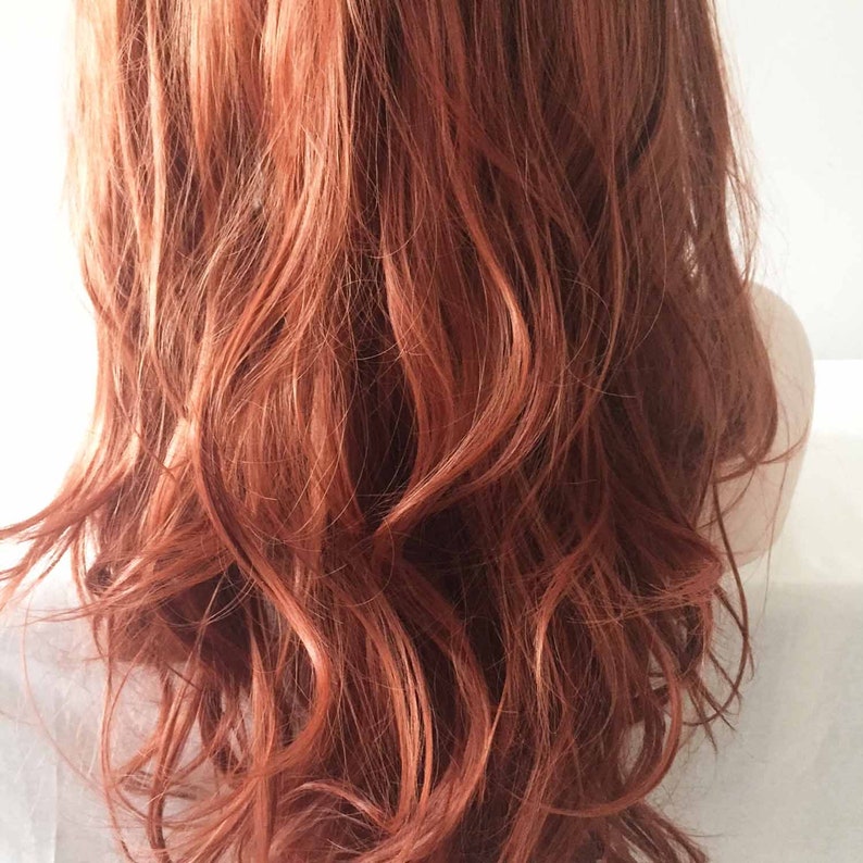 May include: A close-up view of wavy, auburn-colored hair. The hair is styled with loose waves, and the color has a mix of red and brown tones. The hair appears to be healthy and shiny, with a natural look.
