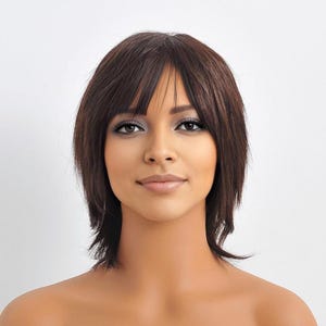 May include: A woman with brown hair and bangs. The hair is styled in a layered, short cut. The woman has brown eyes and is looking directly at the camera. The background is plain white.