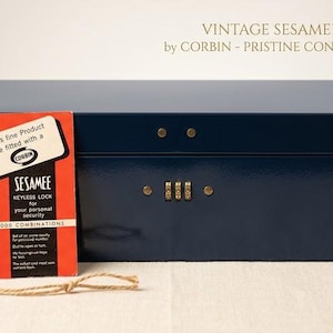 May include: Vintage navy blue Sesamee keyless security box by Corbin, in pristine condition with the original tag. The box features a combination lock and is rectangular. The tag is red with white text.