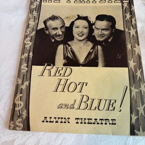 Puede incluir: Programa de teatro vintage para "Red Hot and Blue!" con una foto en blanco y negro de tres actores. El título está en negrita, con "Alvin Theatre" en la parte inferior. La portada tiene símbolos de dólar y diseños de estrellas.