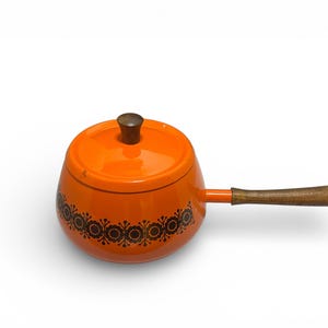May include: An orange enamel saucepan with a lid and a wooden handle. The saucepan has a decorative floral pattern around the base. The lid has a wooden knob.