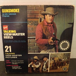 May include: Vintage "Gunsmoke" View-Master reel set. The box features a color image of a man in a cowboy hat holding a gun, with the text "Gunsmoke" and "Talking View-Master Reels." The set includes 21 talking view-master pictures.