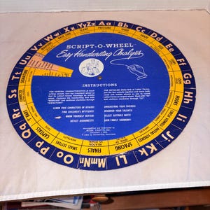 Puede incluir: Un Script-O-Wheel vintage para el análisis de la escritura. La herramienta circular presenta un diseño azul y amarillo con texto e instrucciones. Incluye secciones para márgenes, inclinación, presión y otras características de la escritura.
