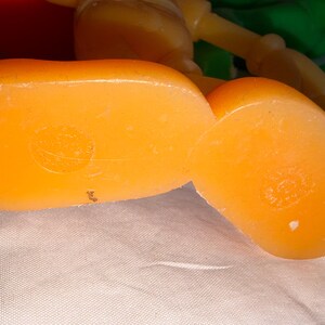 K&ouml;nnte beinhalten: Nahaufnahme von zwei orangefarbenen Spielzeugf&uuml;&szlig;en aus Kunststoff. Die F&uuml;&szlig;e haben eine leuchtende, einfarbige orange Farbe und scheinen Teil einer gr&ouml;&szlig;eren Spielfigur zu sein. Die F&uuml;&szlig;e liegen auf einer wei&szlig;en Oberfl&auml;che. Das Bild ist gut beleuchtet und hebt die glatte Textur des Kunststoffs hervor.