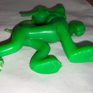 K&ouml;nnte beinhalten: Eine hellgr&uuml;ne Kunststoff-Spielfigur in Krabbelstellung. Das Spielzeug hat eine glatte, gl&auml;nzende Oberfl&auml;che und liegt auf einer wei&szlig;en Oberfl&auml;che. Die Figur hat einen langen Schwanz und gro&szlig;e F&uuml;&szlig;e. Das Spielzeug scheint ein Vintage- oder Retro-Artikel zu sein.