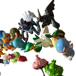May include: A collection of various small plastic character figurines featuring diverse shapes and colors, including blue, green, pink, white, and brown. The figures depict stylized creatures with distinct features like wings, shells, and pointed ears.