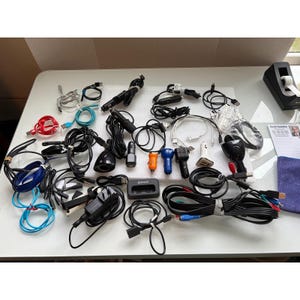 May include: A collection of various electronic accessories including multiple black car chargers, USB cables in red, blue, and black, a small black charging dock, and assorted power adapters. The items are arranged in a group on a white surface.