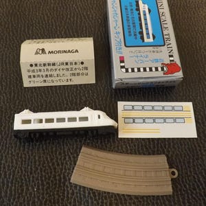May include: A miniature white and black train model with a box labeled "MINI SCALE TRAIN". The set includes a track piece, a sticker sheet, and a box with Japanese text. The train model is a detailed replica.