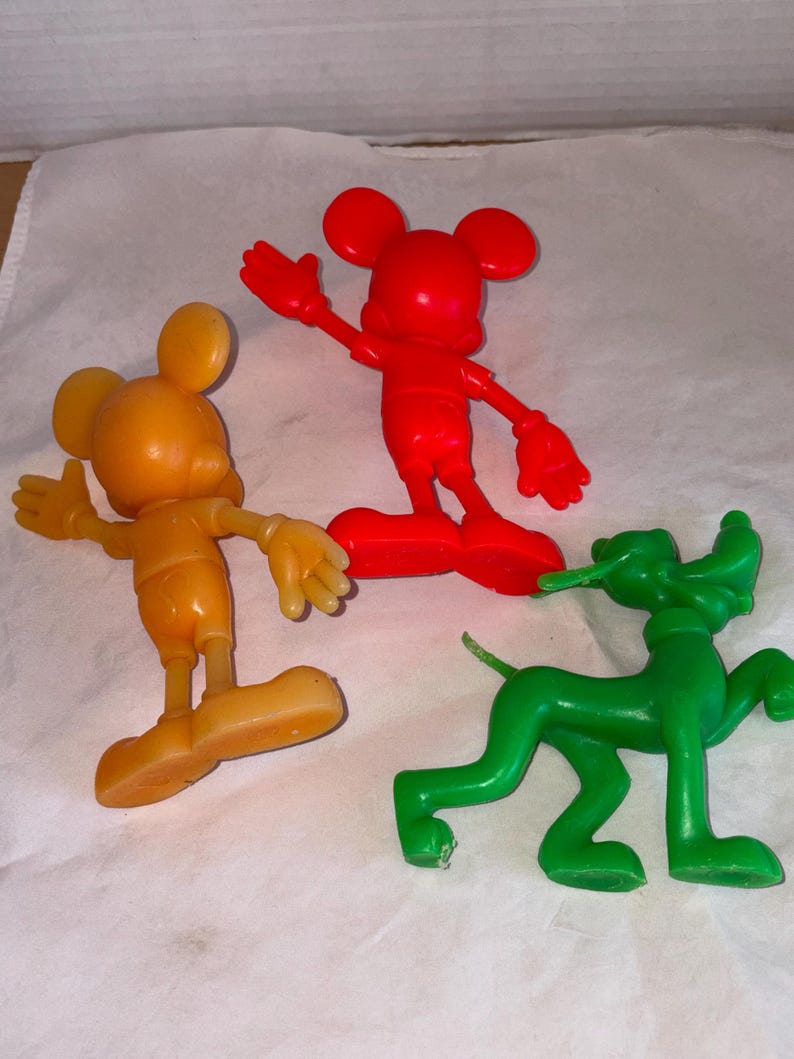 K&ouml;nnte beinhalten: Drei Vintage-Figuren von Disney-Charakteren: eine rote Mickey Mouse, eine orangefarbene Mickey Mouse und ein gr&uuml;ner Pluto. Die Mickey Mouse-Figuren stehen mit ausgestreckten Armen. Die Pluto-Figur befindet sich in einer Laufhaltung.