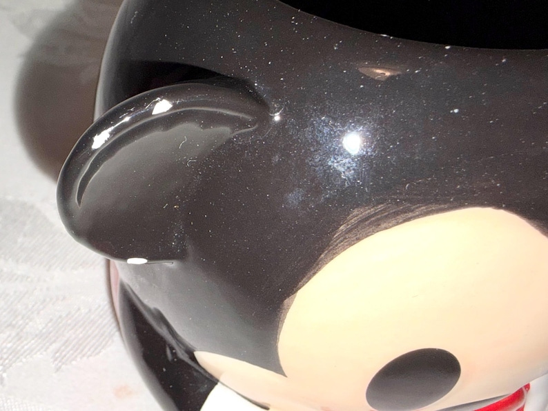 May include: A white ceramic mug with a black handle and the text "But First, Coffee" in a bold, black font. The mug is filled with a dark liquid, likely coffee, and sits on a light-colored surface.