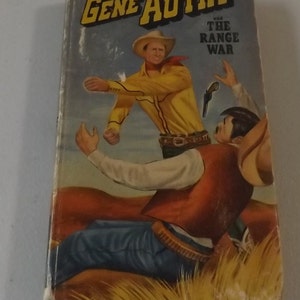 May include: Vintage paperback book titled "Gene Autry and The Range War." The cover art depicts a cowboy in a yellow shirt and hat confronting another cowboy. The background features a desert landscape.