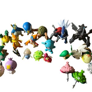 May include: A collection of various small plastic character figurines in diverse colors including blue, green, yellow, pink, and black. The figures feature distinct shapes, some with wings, spikes, or rounded bodies, arranged in a loose group.