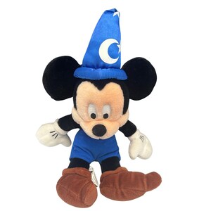 May include: A plush Mickey Mouse toy dressed as a sorcerer, wearing a blue hat with a crescent moon and star, blue shorts, and brown boots. The toy has black ears, a beige face, and white gloves. A classic Disney collectible.